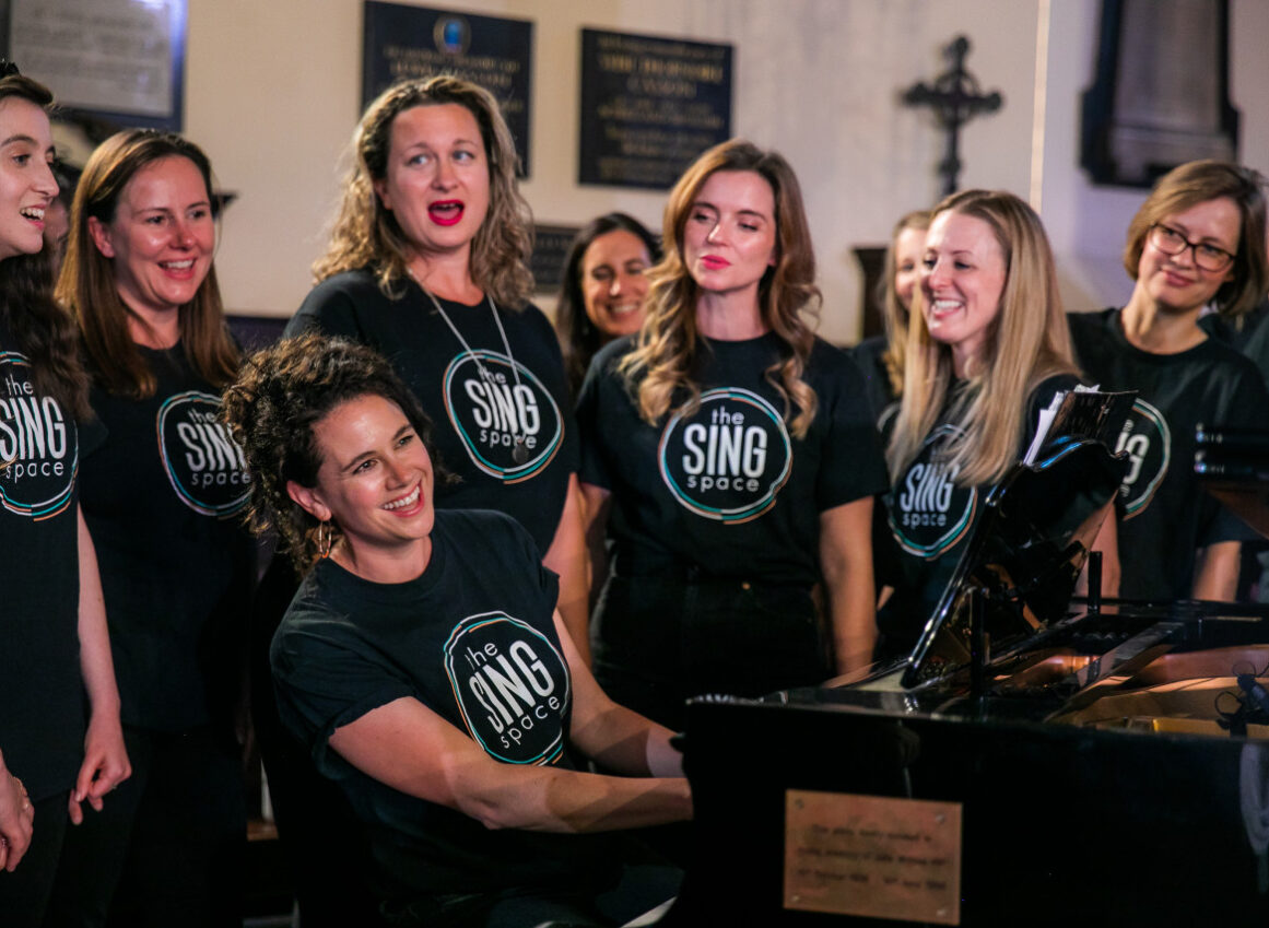 choir singing around a piano