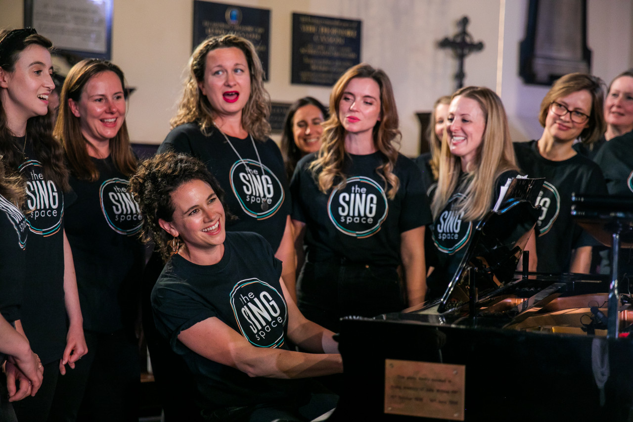 choir singing around a piano